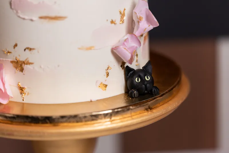Close-up of black cat fondant figurine peeking over the base of the wedding cake