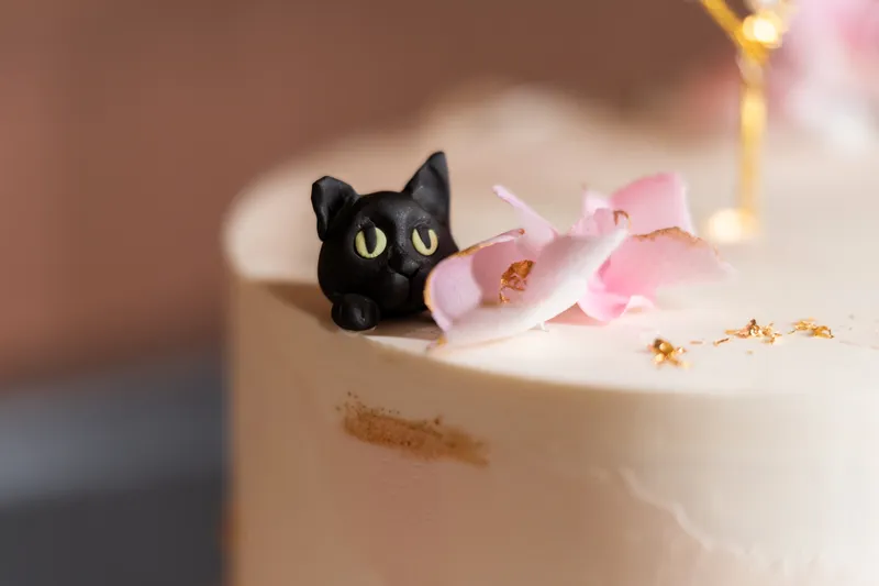 Close-up of black cat fondant figurine on top of the wedding cake with pink fondant petals and gold leaf