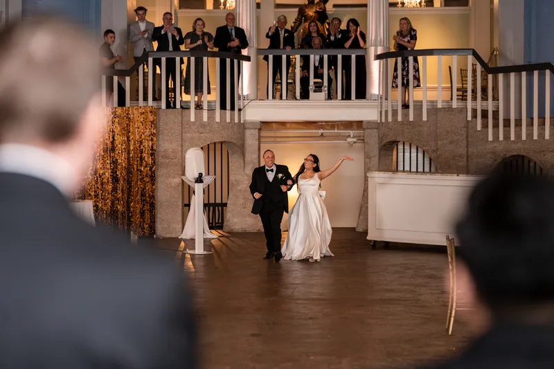 Couple making their grand entrance into the Lightner Museum ballroom with guests watching from the balcony