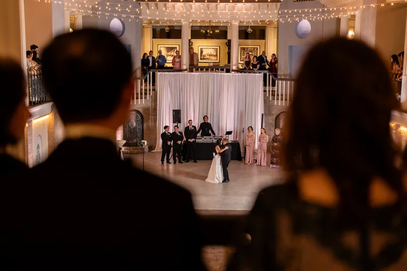 Wide shot of first dance from the balcony with wedding party, DJ, and guests surrounding the dance floor
