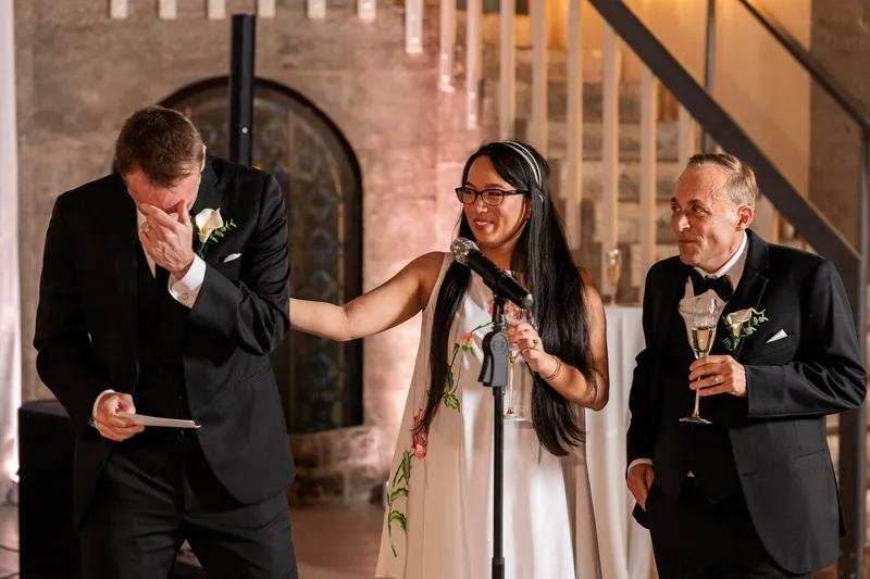 Bride speaking at the microphone while best man tears up during speeches