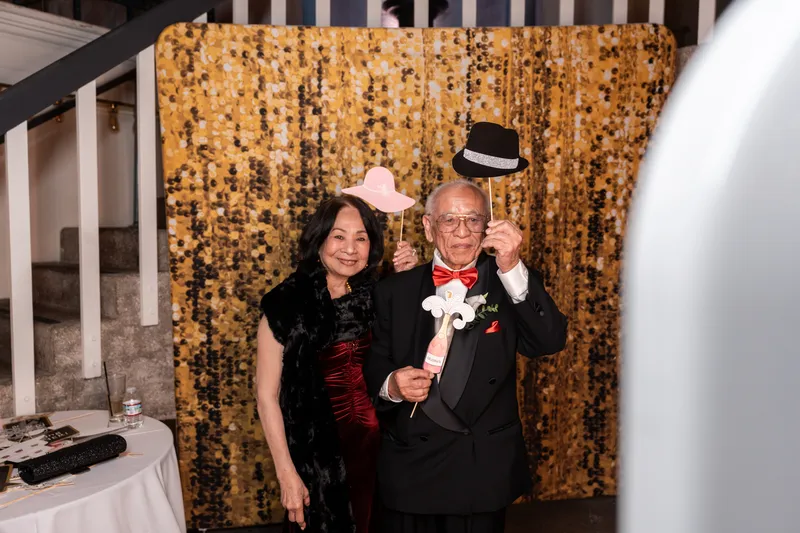 Guests posing with photo booth props at the gold sequin backdrop