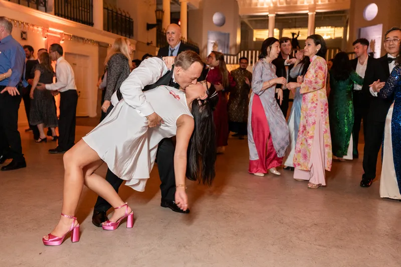 Couple sharing a dip kiss on the dance floor surrounded by guests in ao dai