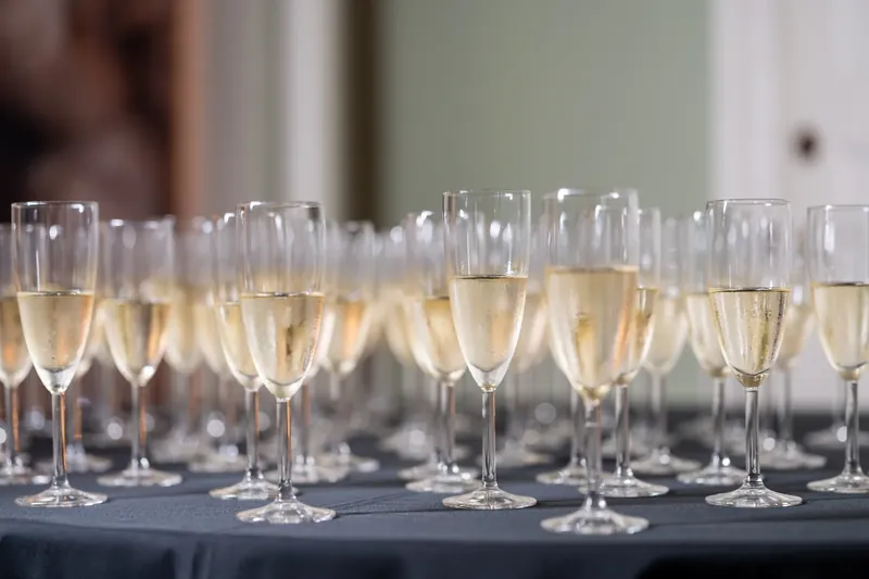 Rows of champagne flutes filled with sparkling wine line a dark table at Lightner Museum.