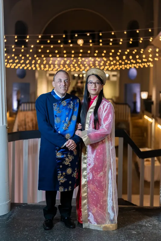 The couple poses under a canopy of warm lights in formal attire at the historic venue.
