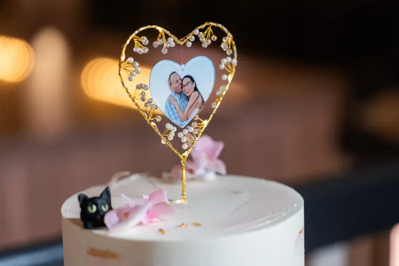 A white cake topped with a gold filigree heart frame holding Elizabeth and Jason's portrait sits at the Lightner Museum.