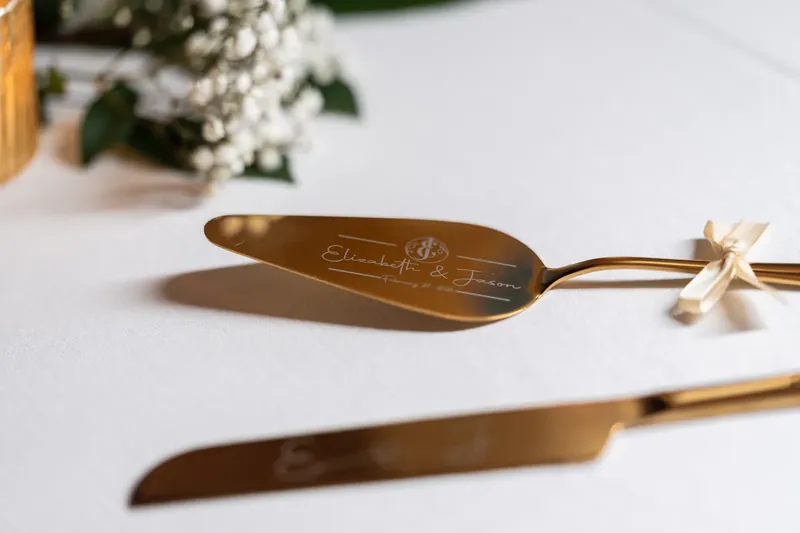 Engraved gold cake server with delicate floral details rests on a white table setting.