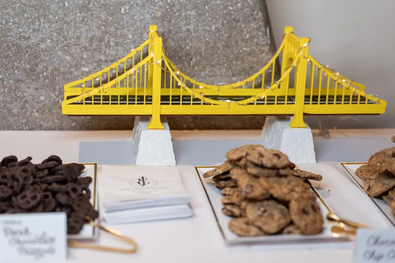 A bright yellow suspension bridge cake topper stands behind an array of chocolate chip cookies on display.