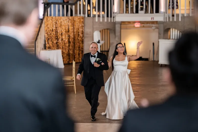 Elizabeth and Jason walk hand in hand down the polished ballroom floor at Lightner Museum as wedding guests watch from either