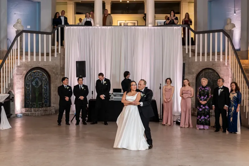 Elizabeth stands alone in her white gown at the center of the Lightner Museum ballroom, surrounded by the wedding party