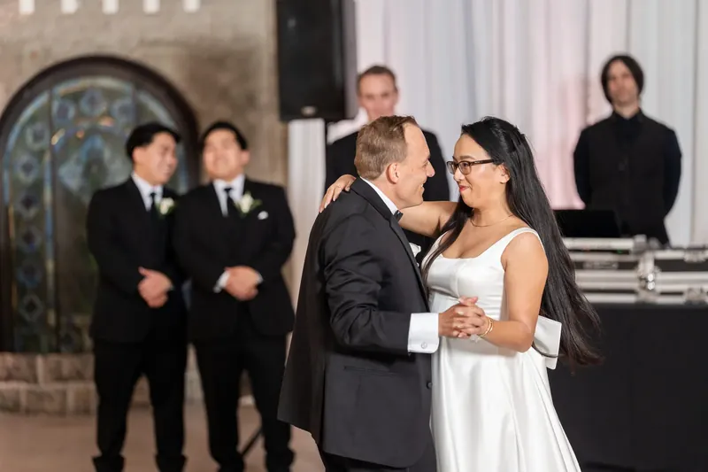 Jason leans in to kiss Elizabeth during their first dance at Lightner Museum, with groomsmen and guests gathered nearby.