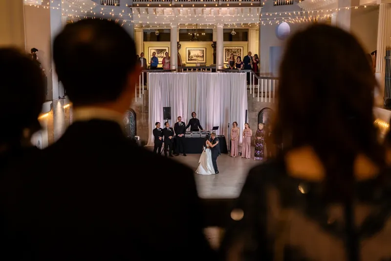Viewed from behind silhouetted guests, Elizabeth and Jason dance together under the ornate chandeliers and draped décor