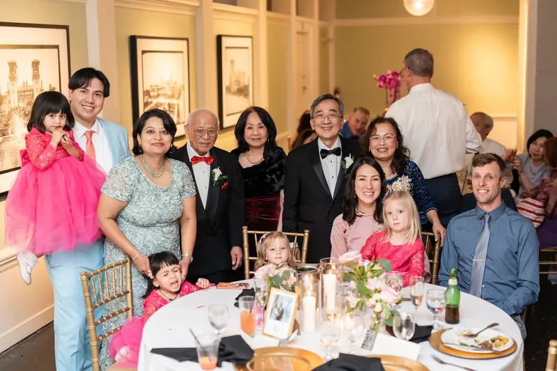 Multiple generations of family members gather around a dining table for a group photo at the reception.