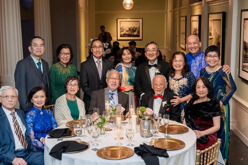 Extended family stands together for a formal portrait beside a table set with gold chargers and glassware.