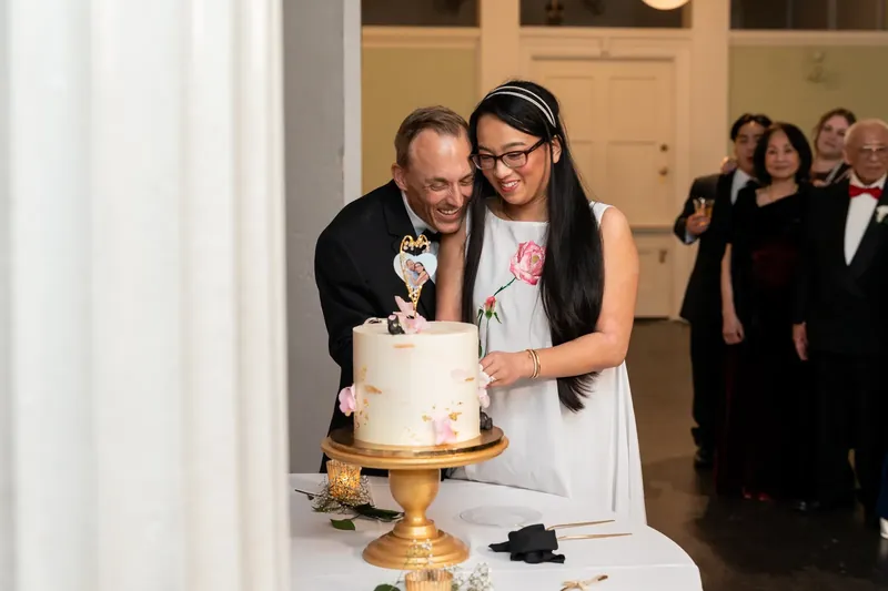 Jason and Elizabeth laugh together while cutting their tiered wedding cake at the Lightner Museum.