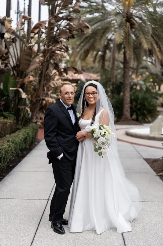 Jason and Elizabeth walk arm in arm down a palm-lined path at the museum, Elizabeth's veil trailing behind them.