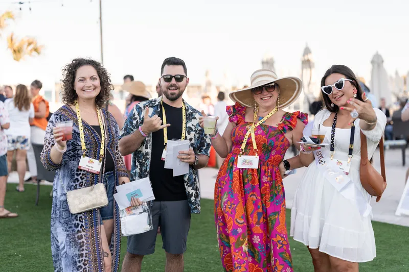 Four guests in colorful, patterned outfits hold drinks and laugh together on the lawn at Embassy Suites St. Augustine Beach
