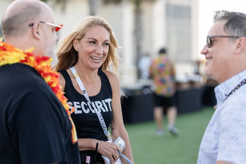 A smiling woman in a black security shirt engages in conversation with two men during the daytime gathering on the hotel