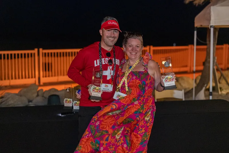 A couple in coordinating red and patterned outfits dance together on an illuminated outdoor stage at night.