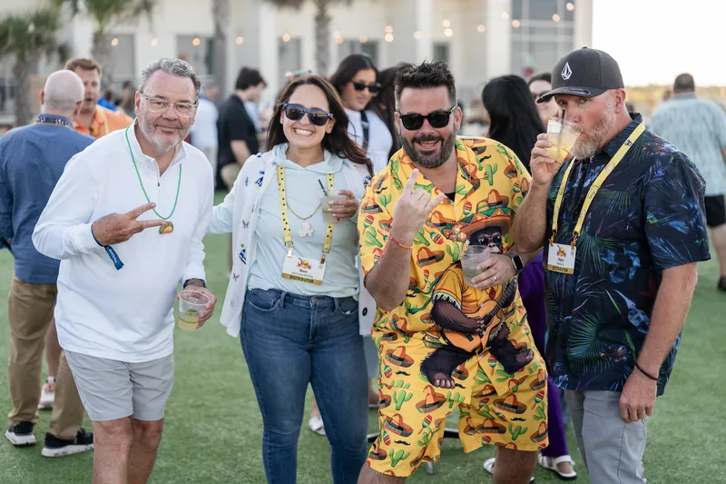 Four guests in bold outfits gather on the lawn at Embassy Suites St. Augustine Beach, including a man in a striking yellow
