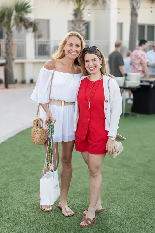 Two smiling guests pose together on the grass, one wearing white and the other in a red sleeveless dress.