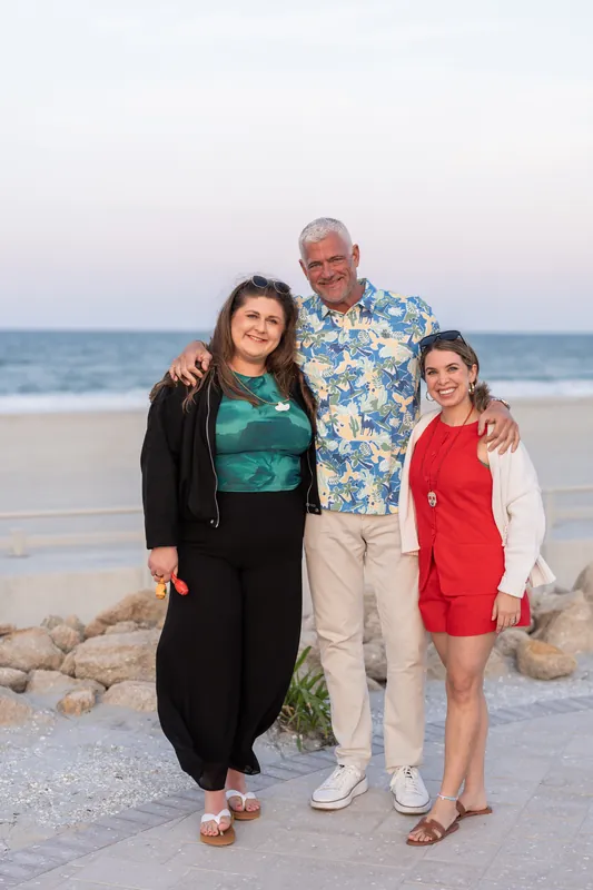 Man in tropical print shirt poses with two women on the sand at Embassy Suites St. Augustine Beach.