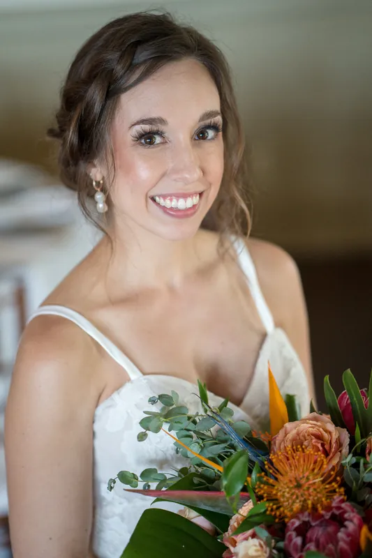 Emma smiles at the camera while holding a bouquet of orange dahlias and blush roses against her white dress.