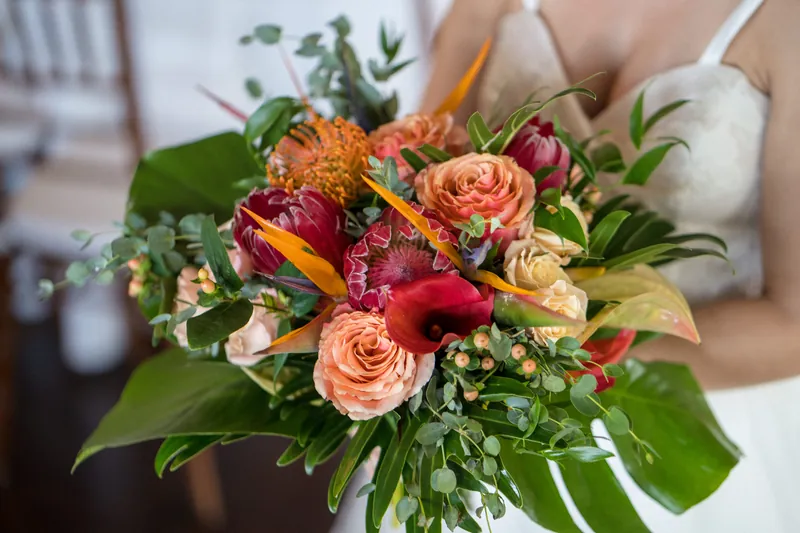 Someone holds a lush bouquet of coral roses, deep red dahlias, and green foliage at Oyster Bay Yacht Club.