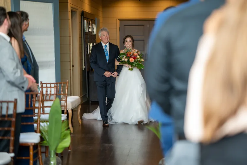 A family member walks Emma down the aisle as Kyle waits at the altar during their ceremony.