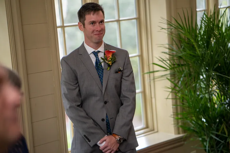 Kyle stands at the altar in a gray suit with a boutonniere, waiting as guests gather for the wedding.