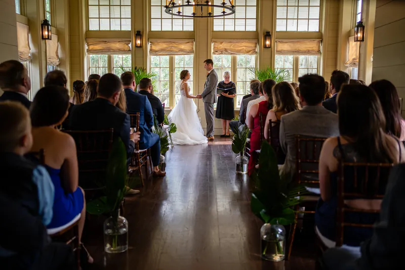 Emma and Kyle exchange vows at the altar during their ceremony at Oyster Bay Yacht Club, with guests seated on either side.