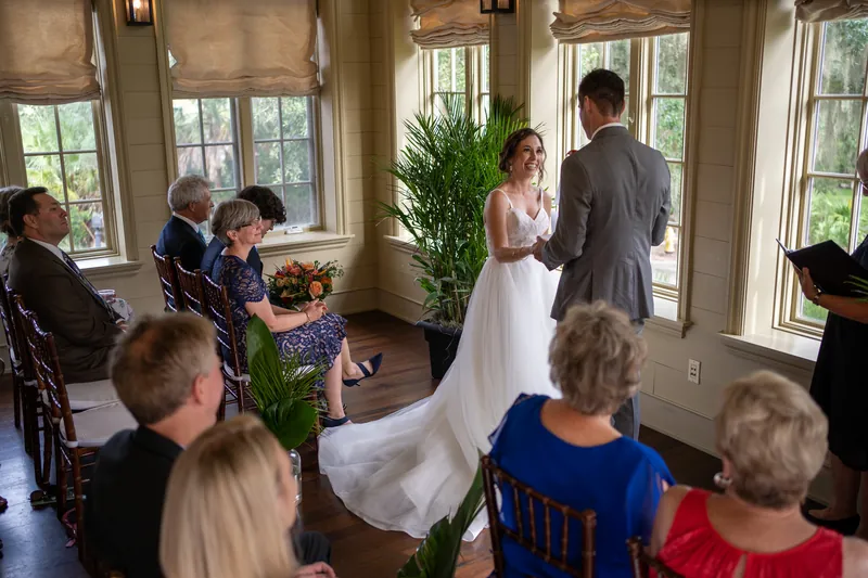 Kyle and Emma face each other during their ceremony while family members watch from nearby seats in the windowed room.