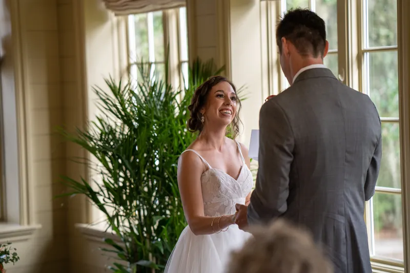 Emma gazes at Kyle with a smile as they stand together in front of large windows filled with natural light.