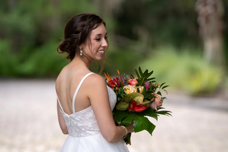 Emma glances over her shoulder in her white gown, clutching her red and orange floral bouquet in soft evening light.