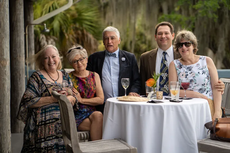 Five family members stand together at a white-clothed high-top table with tropical palms visible in the background.