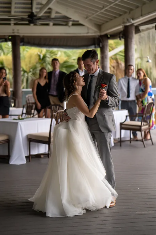 The couple slow-dances on the covered deck surrounded by seated and standing guests at their reception.