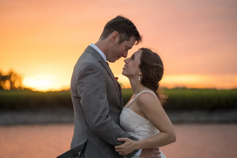 Kyle and Emma embrace closely as the sun dips toward the horizon, their silhouettes framed against the glowing water.
