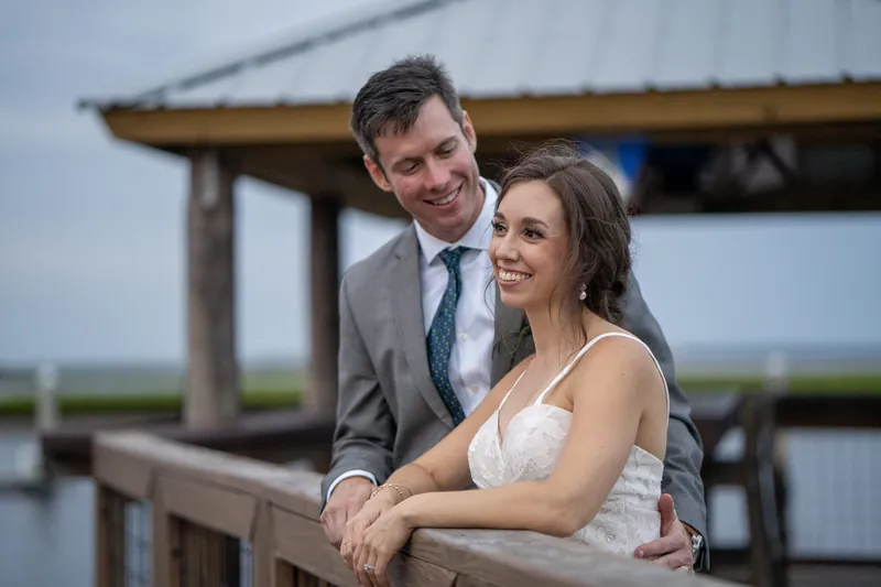 Kyle and Emma lean against a railing on a covered dock, both smiling as they look out over the water.