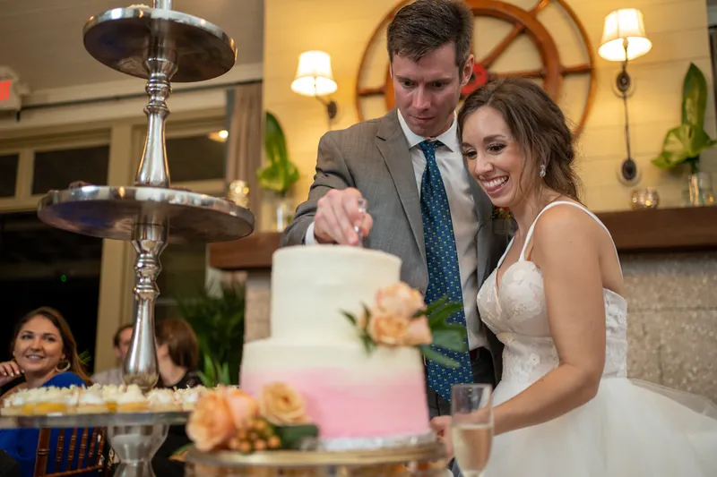 Kyle and Emma cut their pink ombré wedding cake as guests watch from nearby tables.