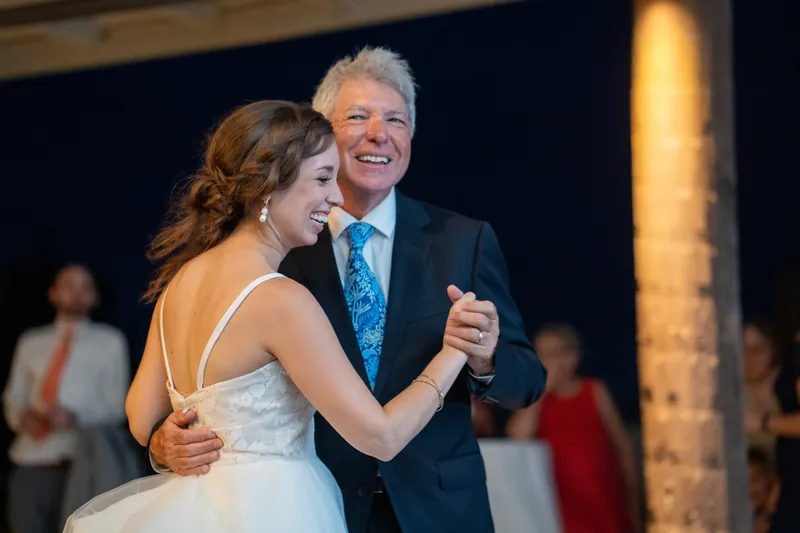 Emma dances with an older man in a blue tie, both smiling as they move across the reception floor.