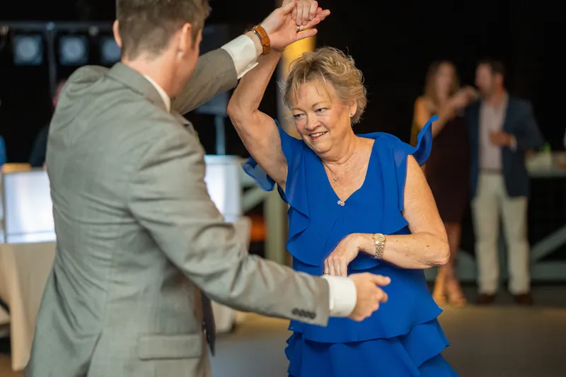 A man in a gray jacket spins a woman in a blue sleeveless dress on the dance floor at Oyster Bay Yacht Club.