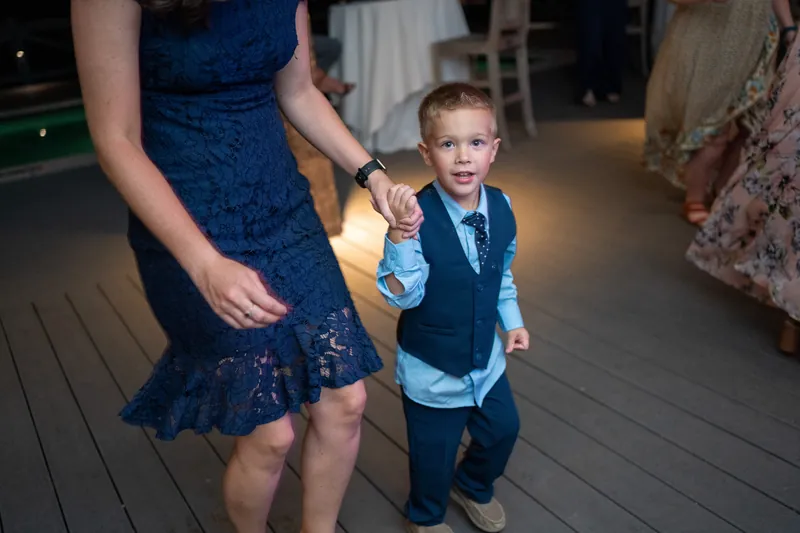 A young child in a blue vest walks hand-in-hand with a woman in a navy sequined dress across the venue floor.