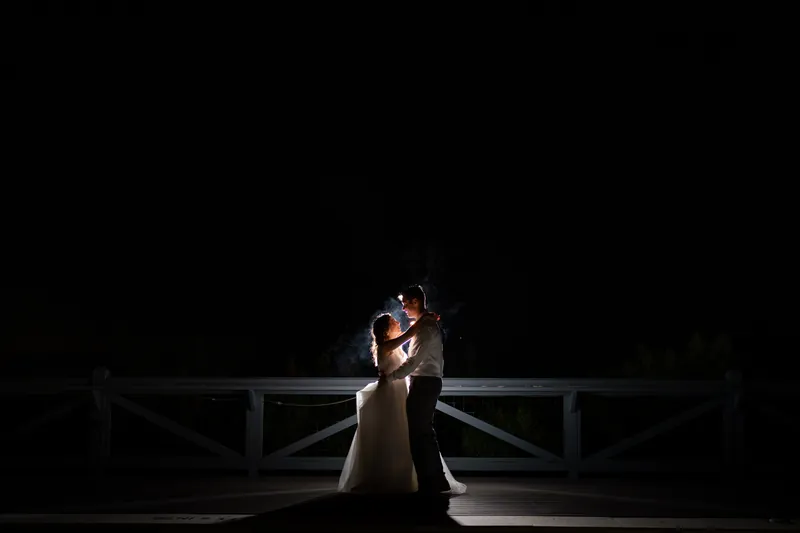 Emma and Kyle embrace on a waterfront dock under soft evening light at Oyster Bay Yacht Club.