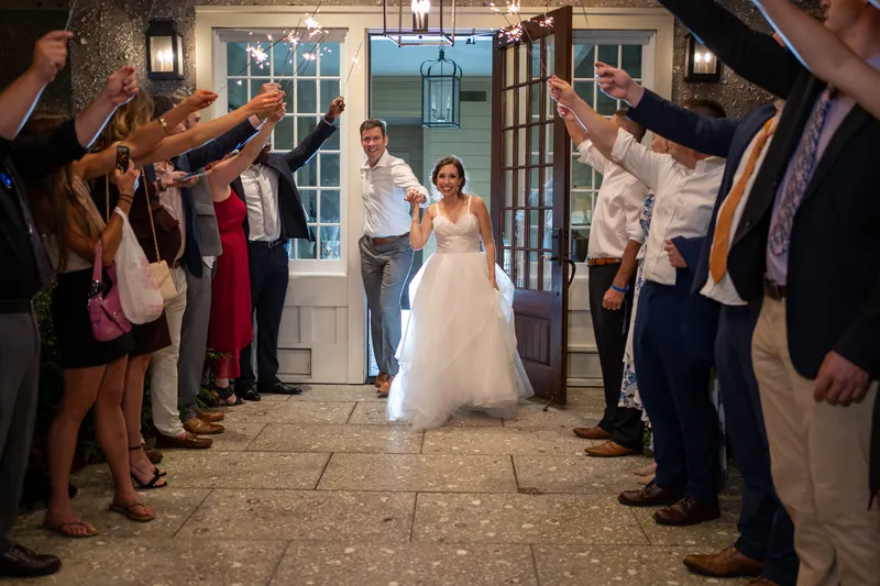 Emma walks down an aisle lined with guests holding sparklers at Oyster Bay Yacht Club, wearing a white gown.