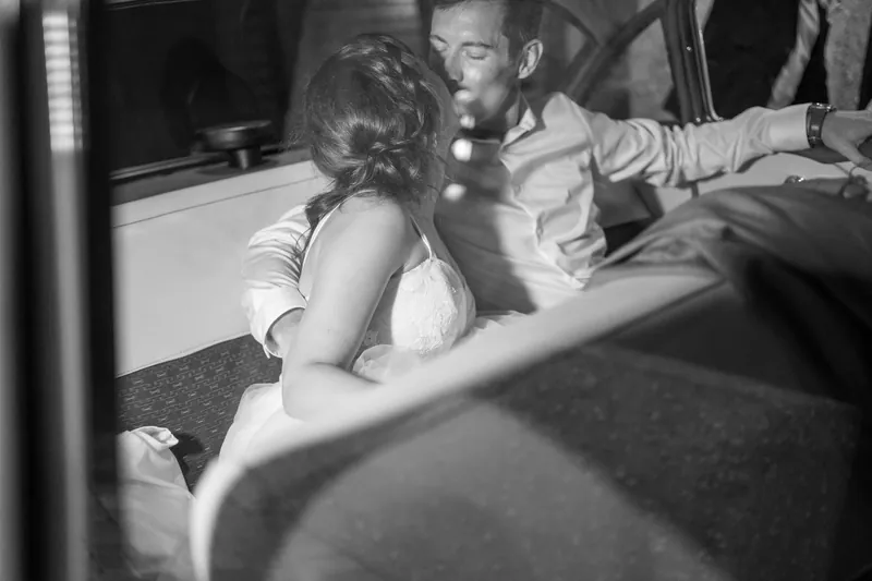 Emma and Kyle sit close together in the back seat of a vintage car, sharing an intimate moment in black and white.