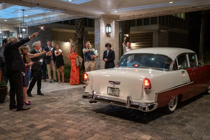 Guests gather around a classic 1950s two-tone car parked in the venue's covered entrance at Oyster Bay Yacht Club.