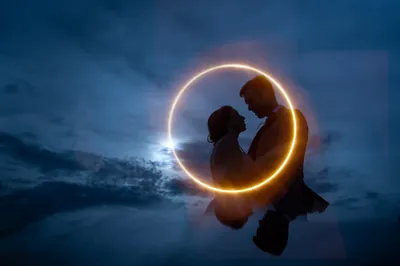 Two silhouettes lean toward each other within a glowing circular light ring against a twilight sky.