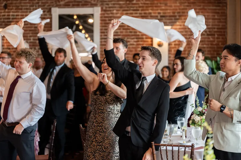 Wedding guests raise white napkins and cheer as the newlyweds walk through The White Room's brick interior during their reception.