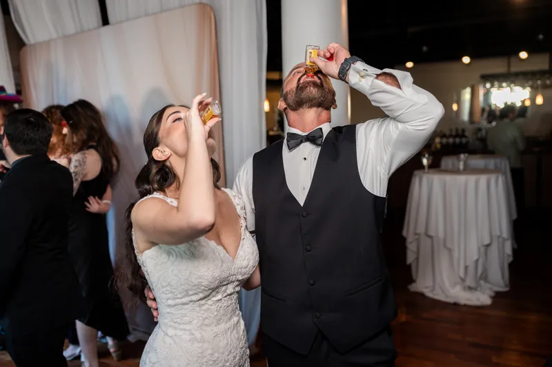 Two people in wedding attire toss their heads back mid-celebration on the dance floor at The White Room, surrounded by guests.
