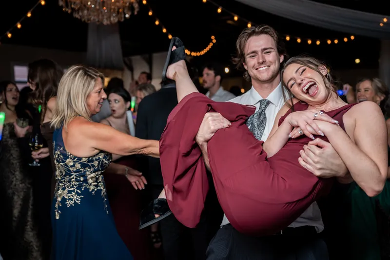 A person in a maroon suit gets lifted by two guests in a playful moment on the dance floor at The White Room.